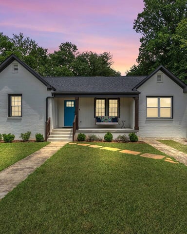 Modern single-story home exterior with patio, mint-green door, white desk setup, and tree-lined yard
